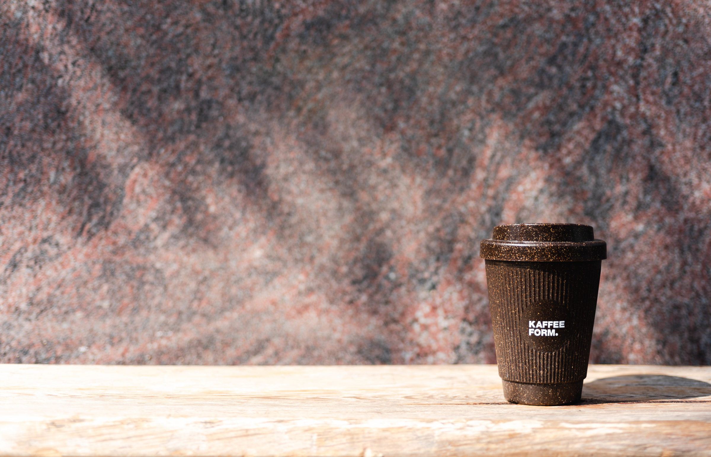 Weducer Cup mit Kaffeeform Logo auf einem Holztisch mit Steinhintergrund