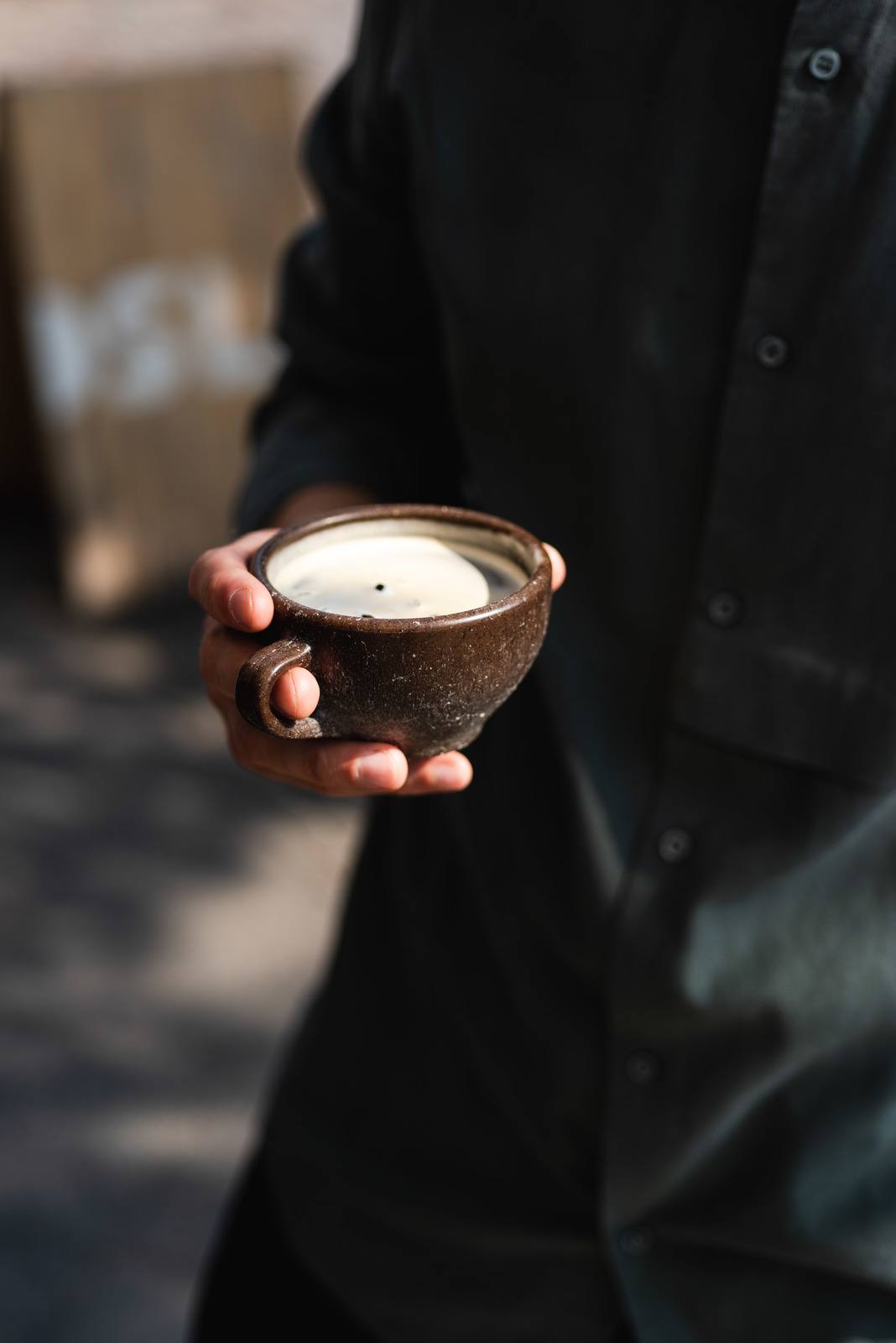 Person mit schwarzem Hemd hält einen Kaffeeform Cup mit einem schwarzen Kaffee