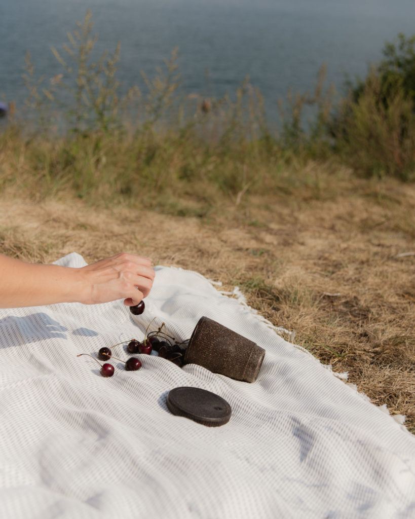 Picknickdecke mit dem Weducer Cup gefüllt mit Kirschen neben dem Weducer Cap