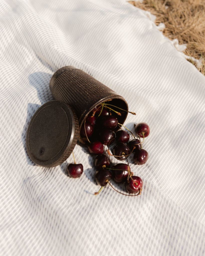 Picknickdecke mit dem Weducer Cup gefüllt mit Kirschen neben dem Weducer Cap