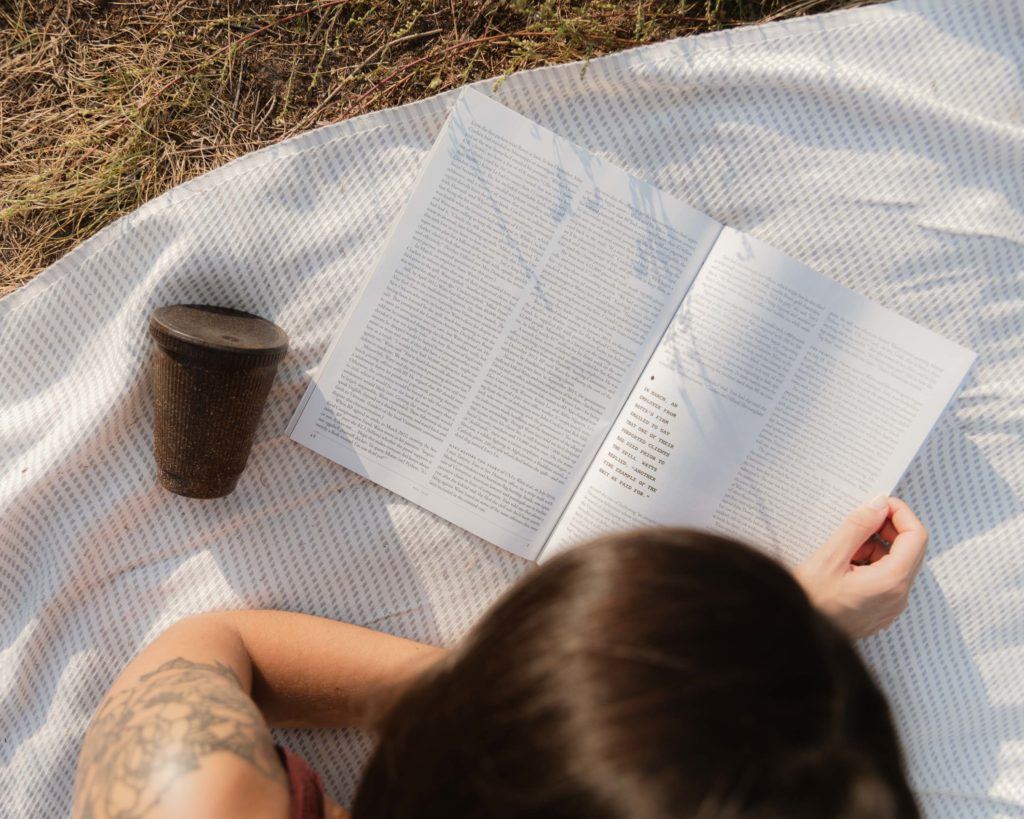 Person liest ein Magazin neben dem Weducer mit Cap auf einer Picknickdecke